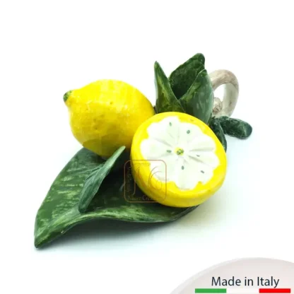 Bugia con due limoni, uno intero e uno aperto, adagiata su foglie con fiorellino e manico.